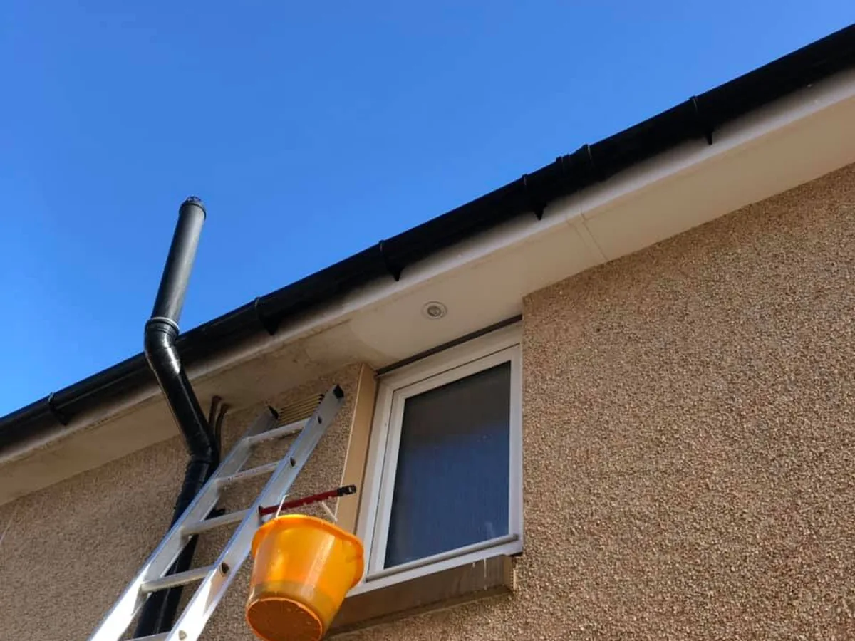 Mid-job: a ladder up to the soffit of a house in Bishopton, a downlight being fitted and the cable clipped along the wall